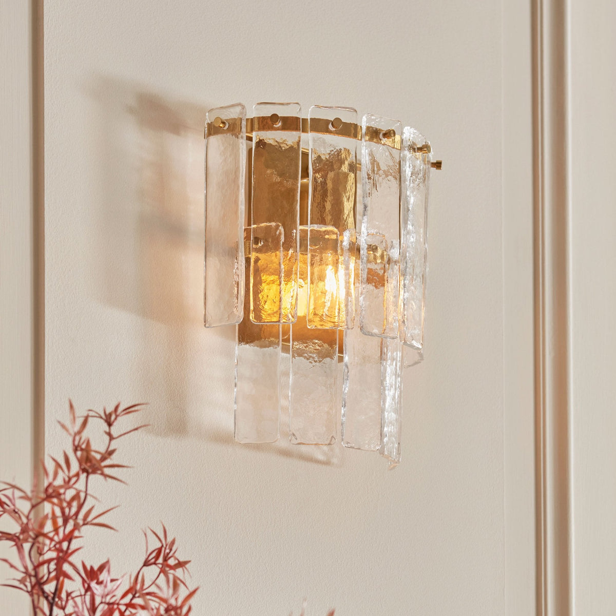 A close-up of the sconce, highlighting its unique glass and brass design with warm light.