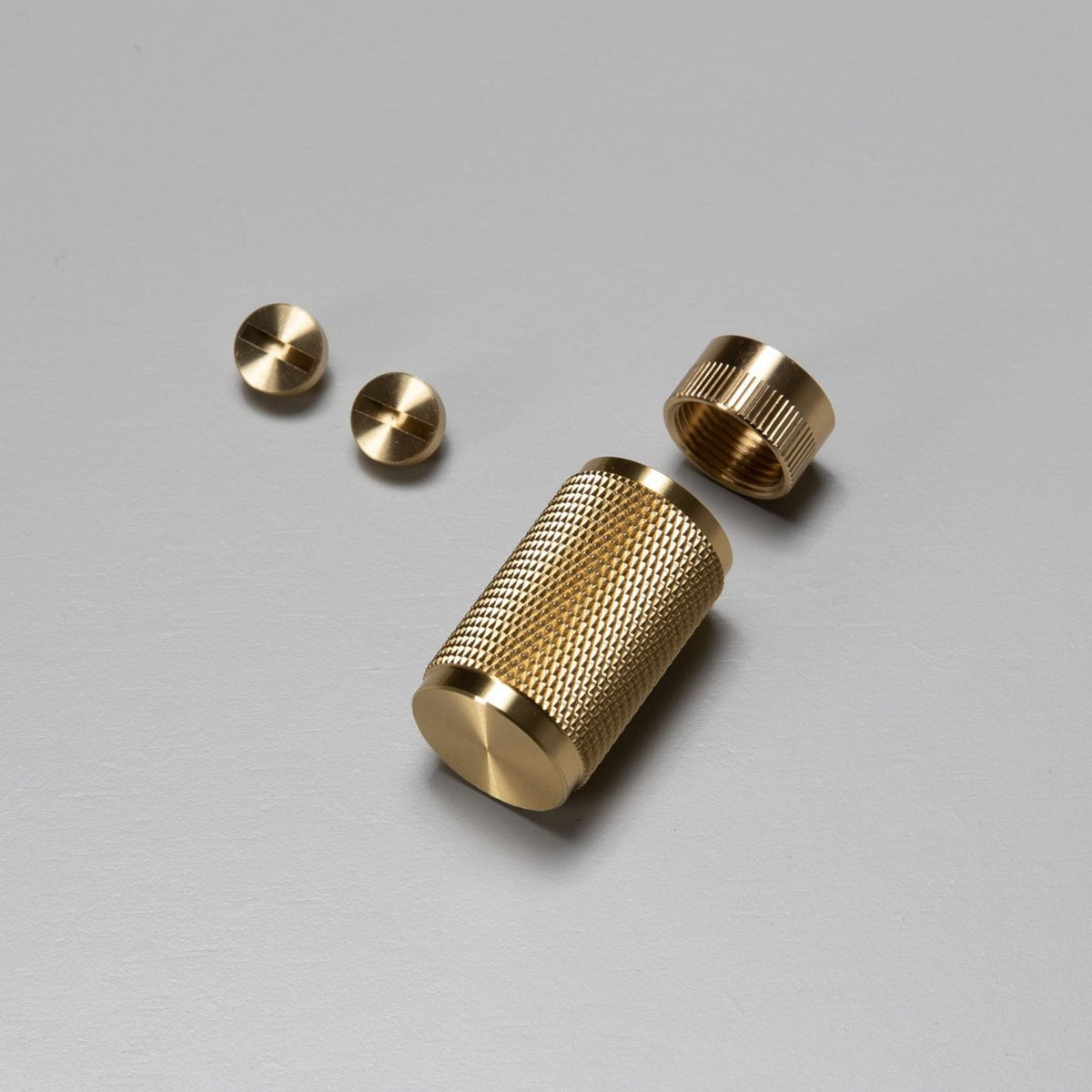 Brass knurled cylinder, a threaded cap, and two flat-head screws on a gray surface.