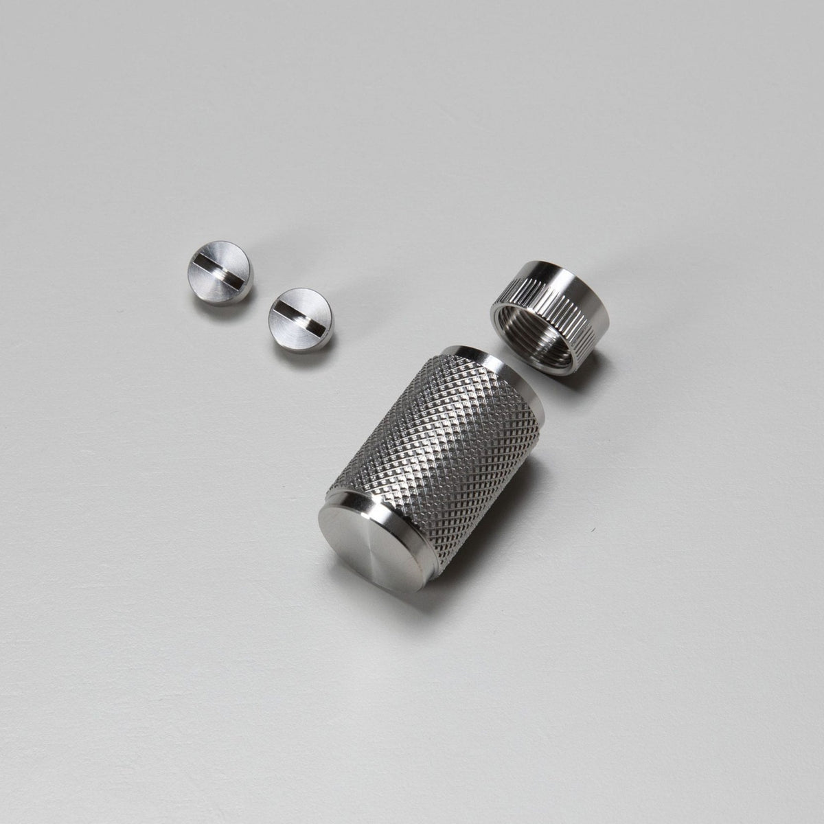 Two small screws and a textured metal cylinder with a threaded cap on a light gray surface.