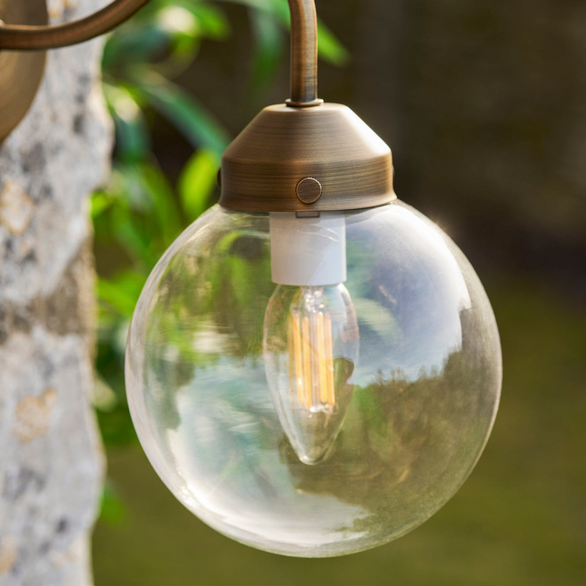 Globe-shaped outdoor light fixture with clear glass cover and visible bulb against a natural background.