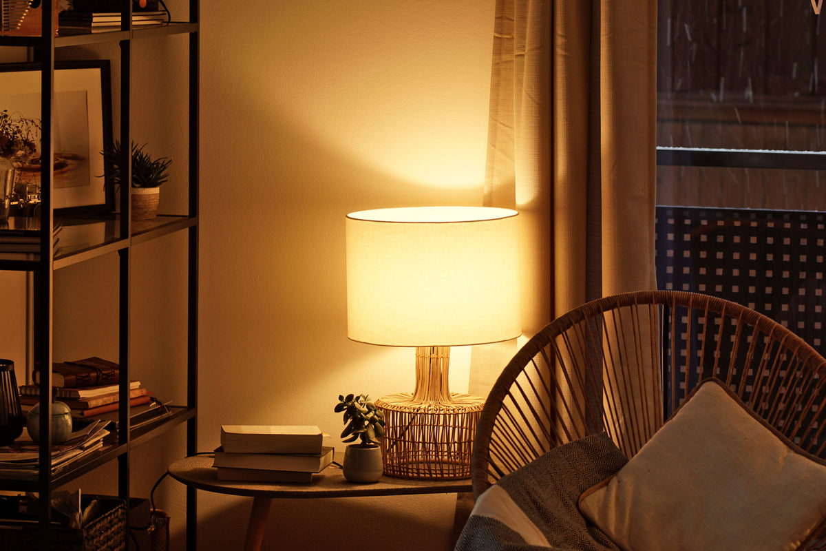 A warm, inviting living room with a table lamp, a bookshelf, and a wicker chair