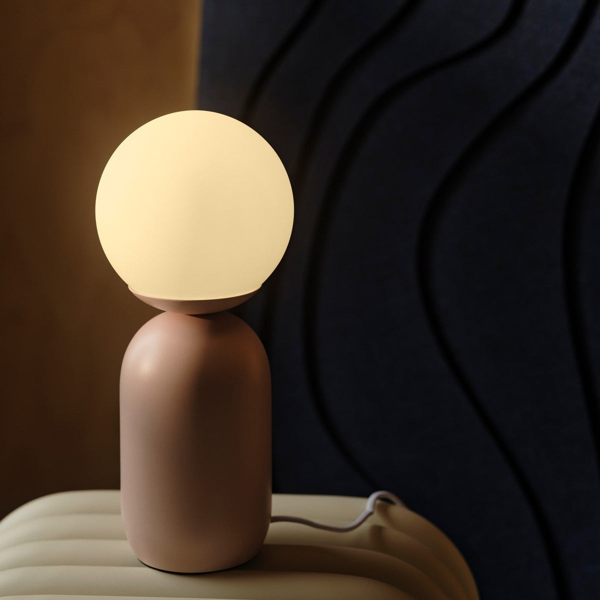 Pink table lamp with a glowing spherical bulb on a light-colored surface