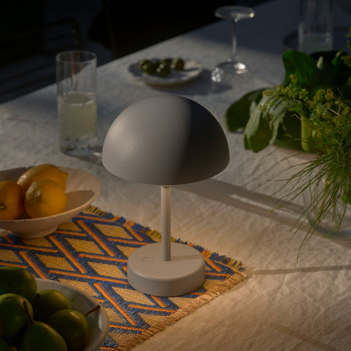Grey dome-shaped lamp on a table with lemons, green fruit, and a drink