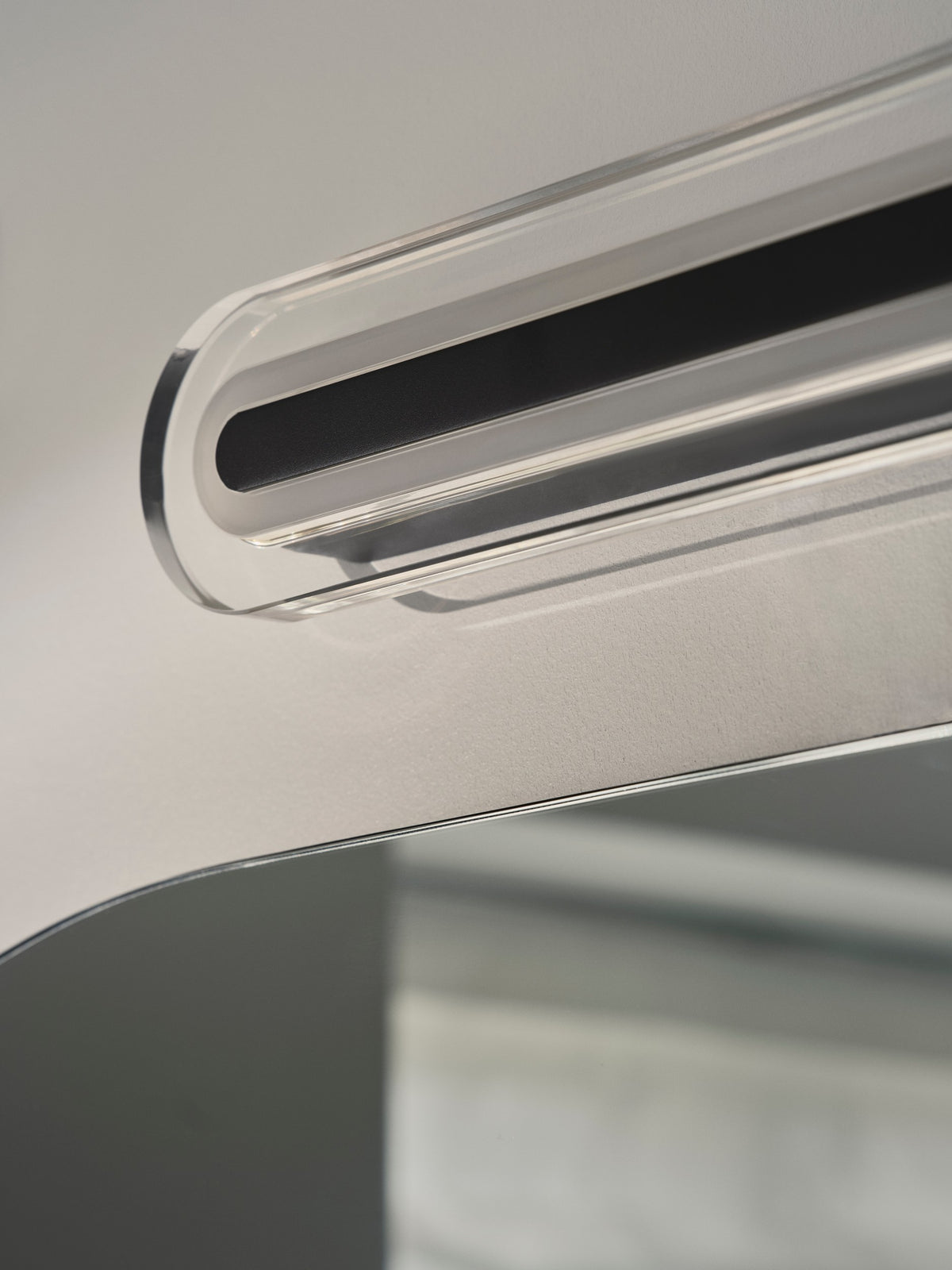 Close up of a clear acrylic light fixture with a black strip, mounted above a mirror