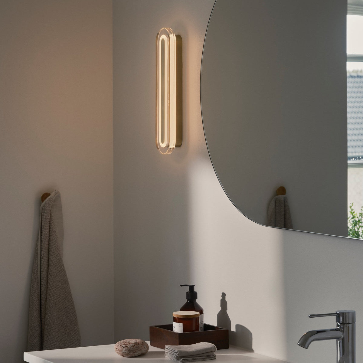 Bathroom vanity with a lit wall sconce, round mirror, and sink with chrome faucet