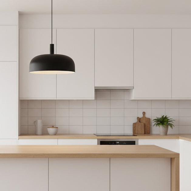 Black pendant light hanging over a light wood kitchen island in a white kitchen