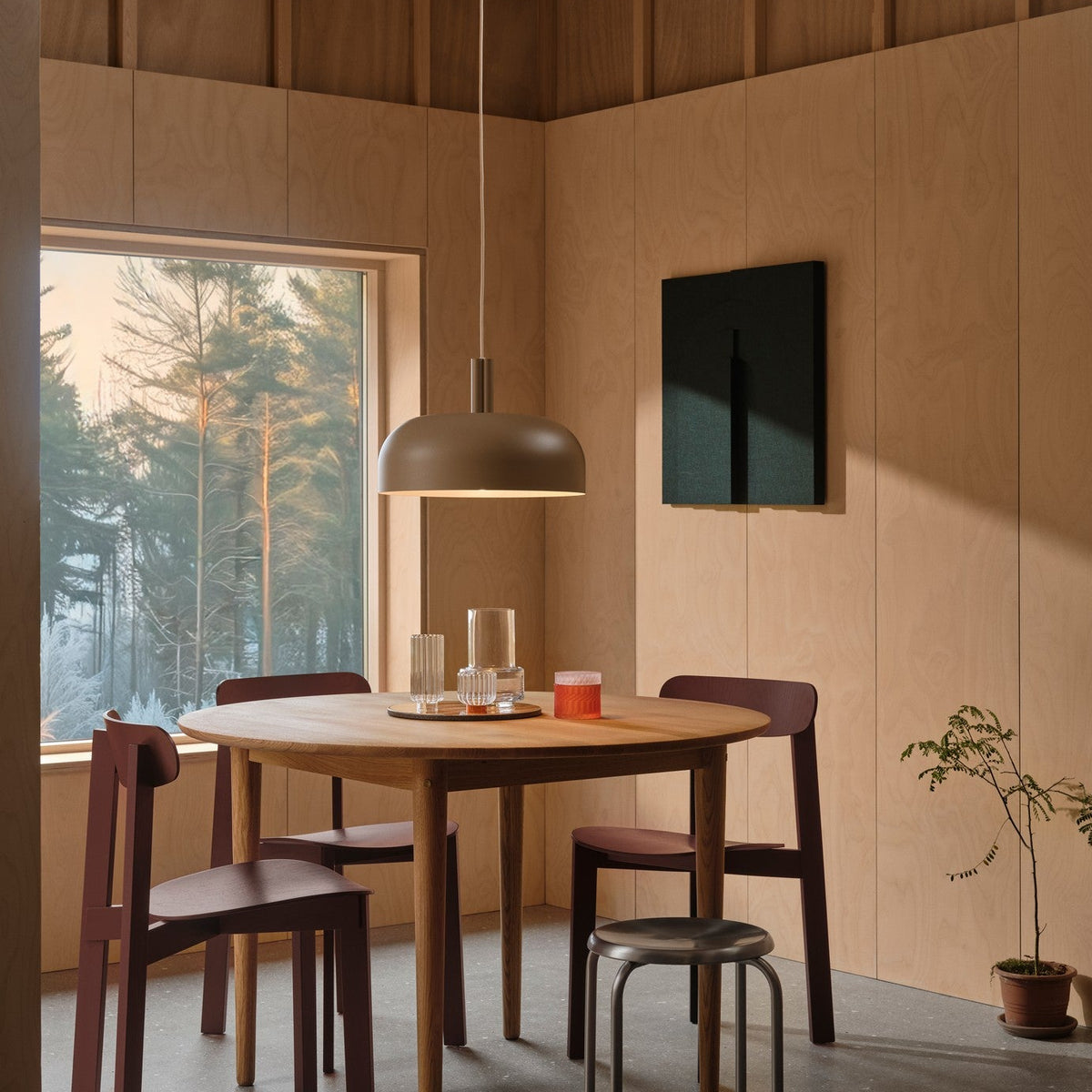 Dining room with a round wooden table, four chairs, a pendant light, and a window overlooking a forest