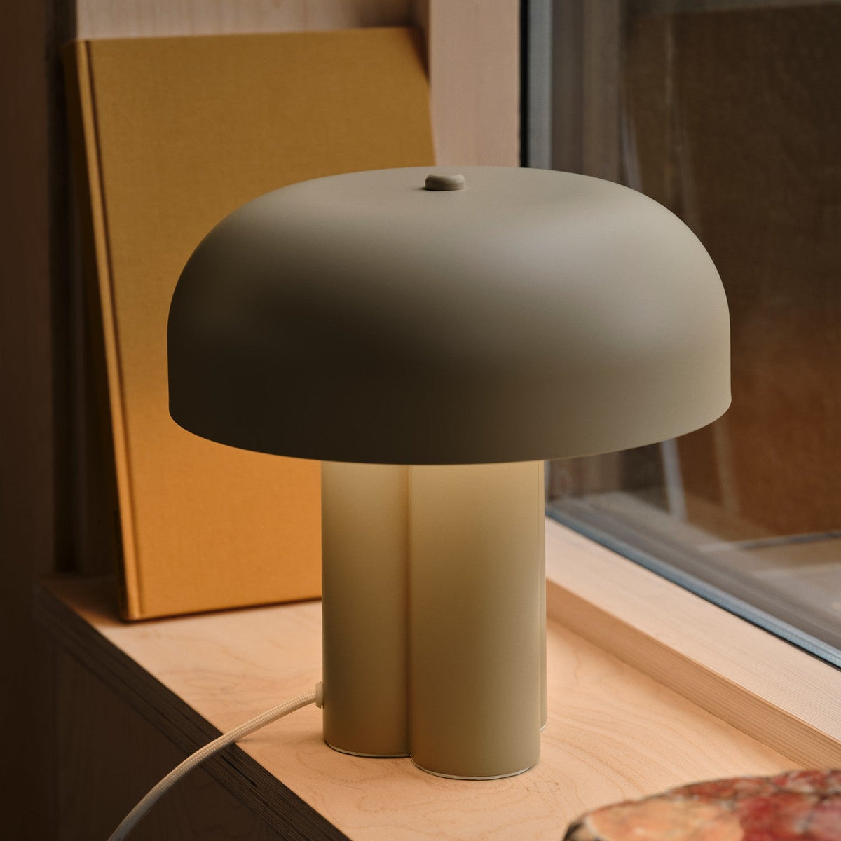 Mushroom-shaped table lamp with a matte olive green shade and base, on a light wood surface