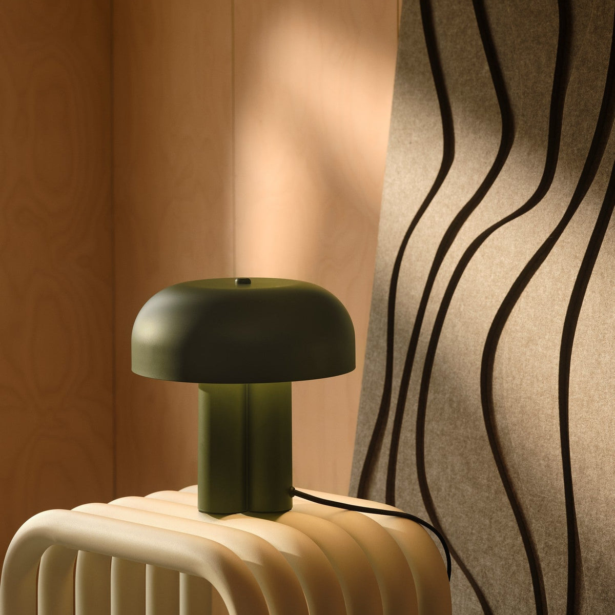 Green table lamp on a cream-colored ribbed surface, with a wavy textured wall panel in the background
