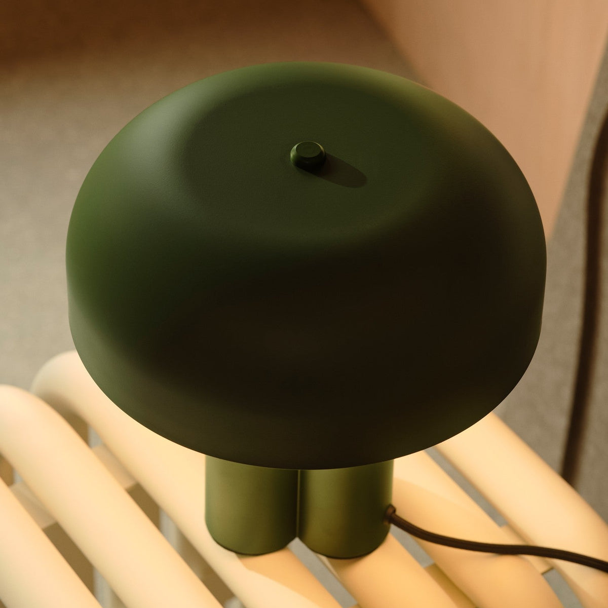 Dark green mushroom-shaped table lamp with a black cord on a light-colored slatted surface