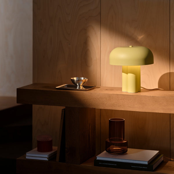 Lime green table lamp on a wooden shelf with a silver bowl and books
