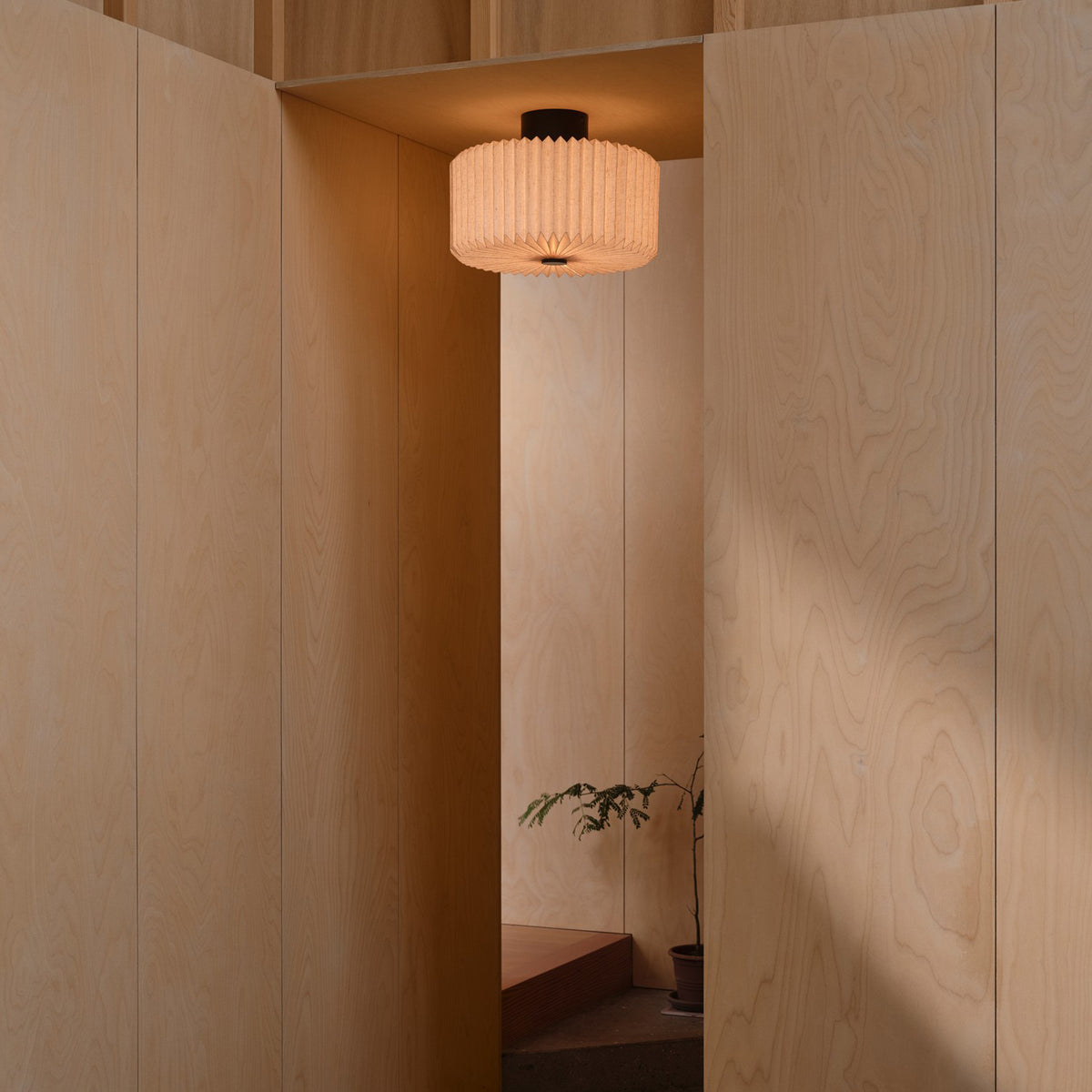 A light wood room with a pleated circular light fixture hanging from the ceiling