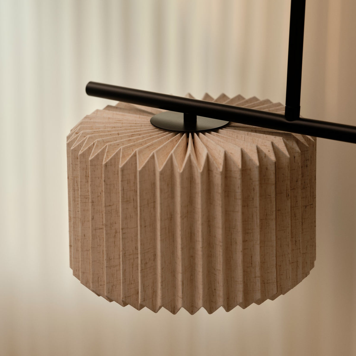 Close up of a beige pleated fabric lampshade with a black metal rod passing through its center