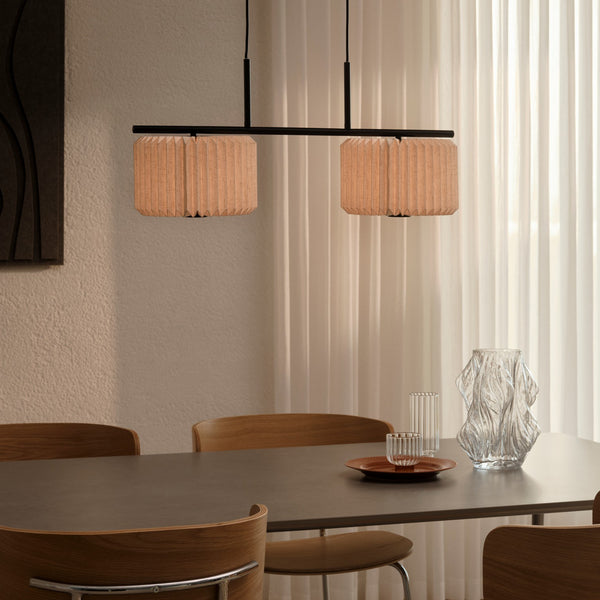 Two pendant lights with pleated wooden shades hang above a dining table with wooden chairs