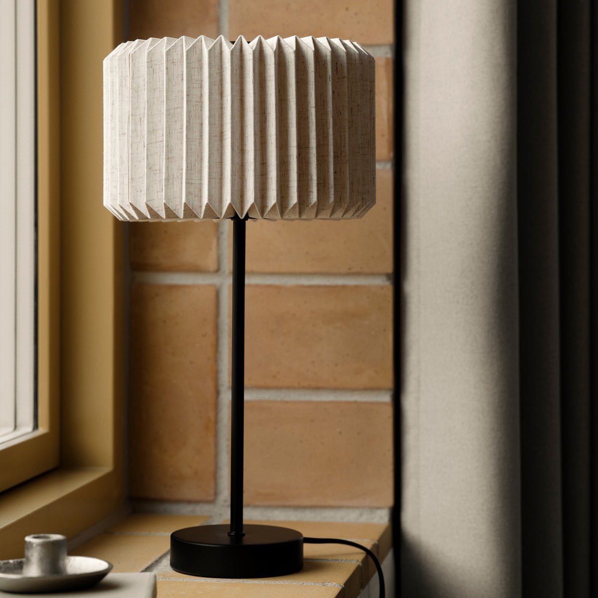 Table lamp with a pleated fabric shade and a black metal base, sitting on a window ledge