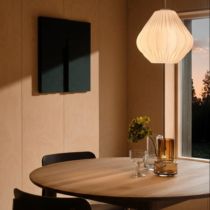 Dining room with a round wooden table, black chairs, a white pendant light, and a dark green acoustic panel