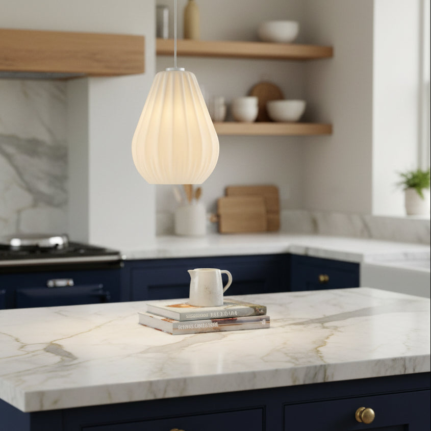 A white fluted pendant light hangs above a kitchen island with a marble countertop and dark blue cabinets