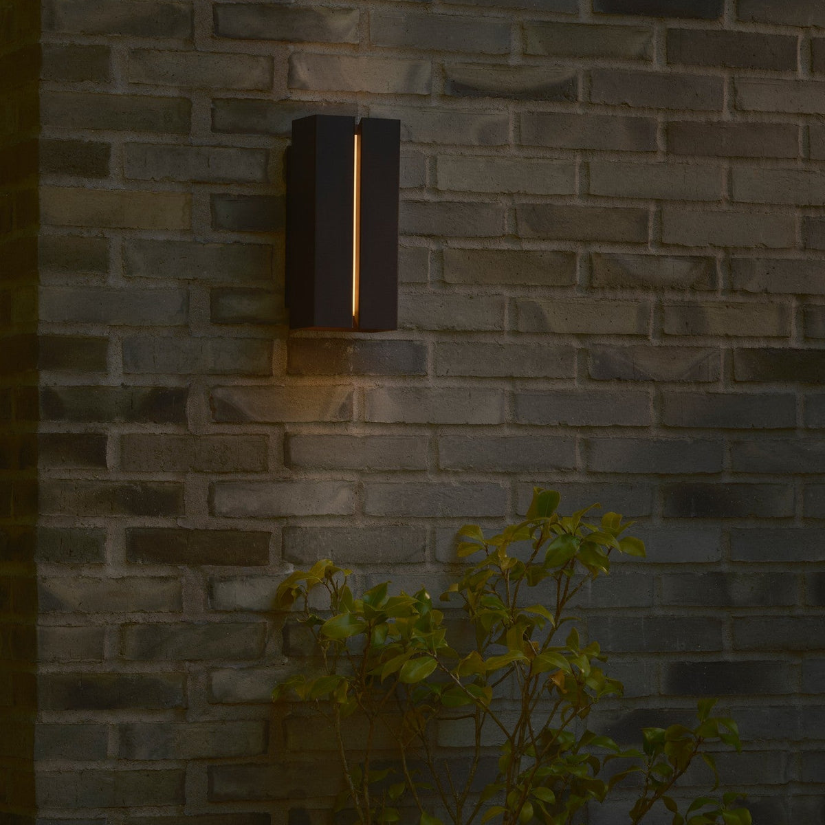 Black rectangular outdoor wall light with a vertical light strip on a grey brick wall