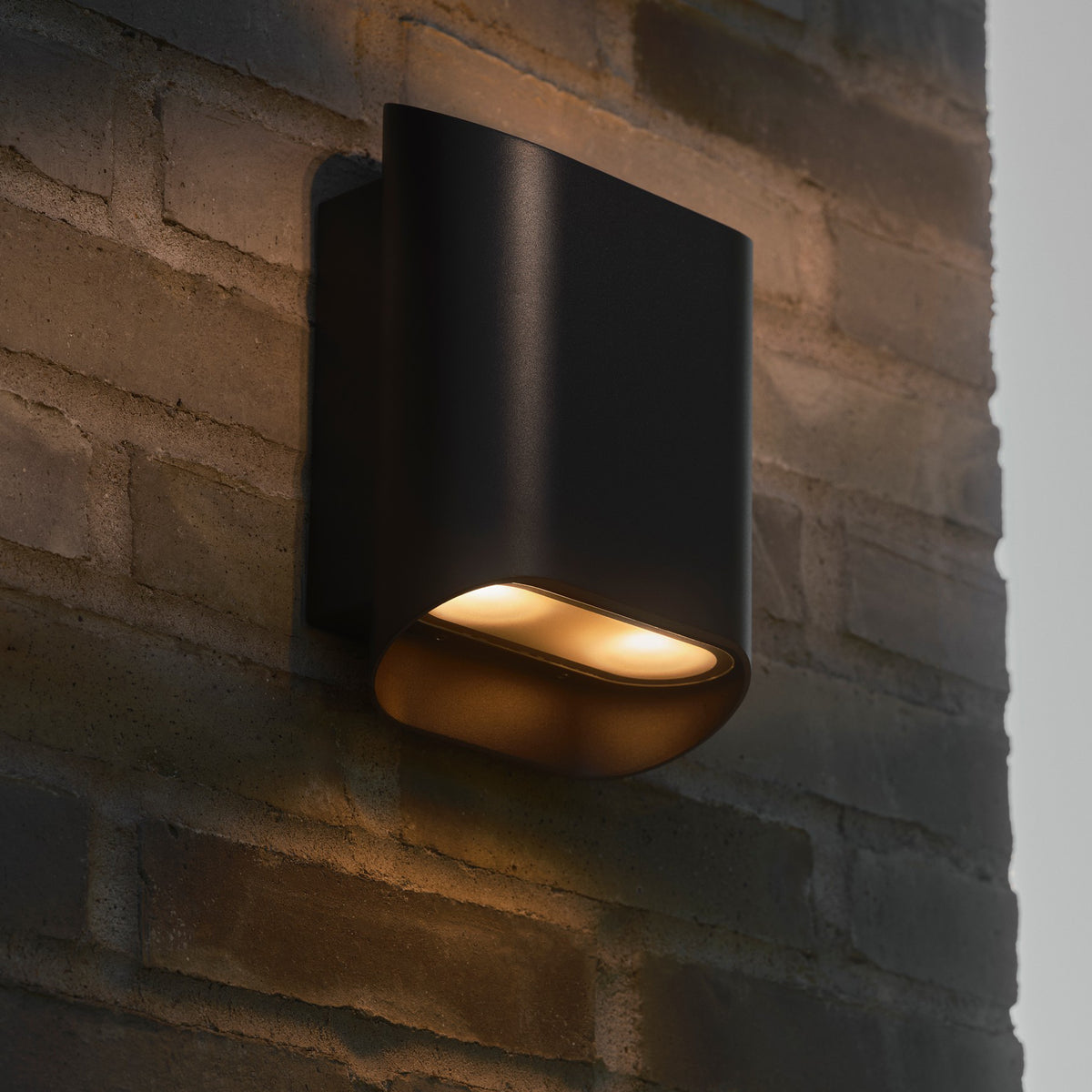 Black outdoor wall light with warm glow on a brick wall