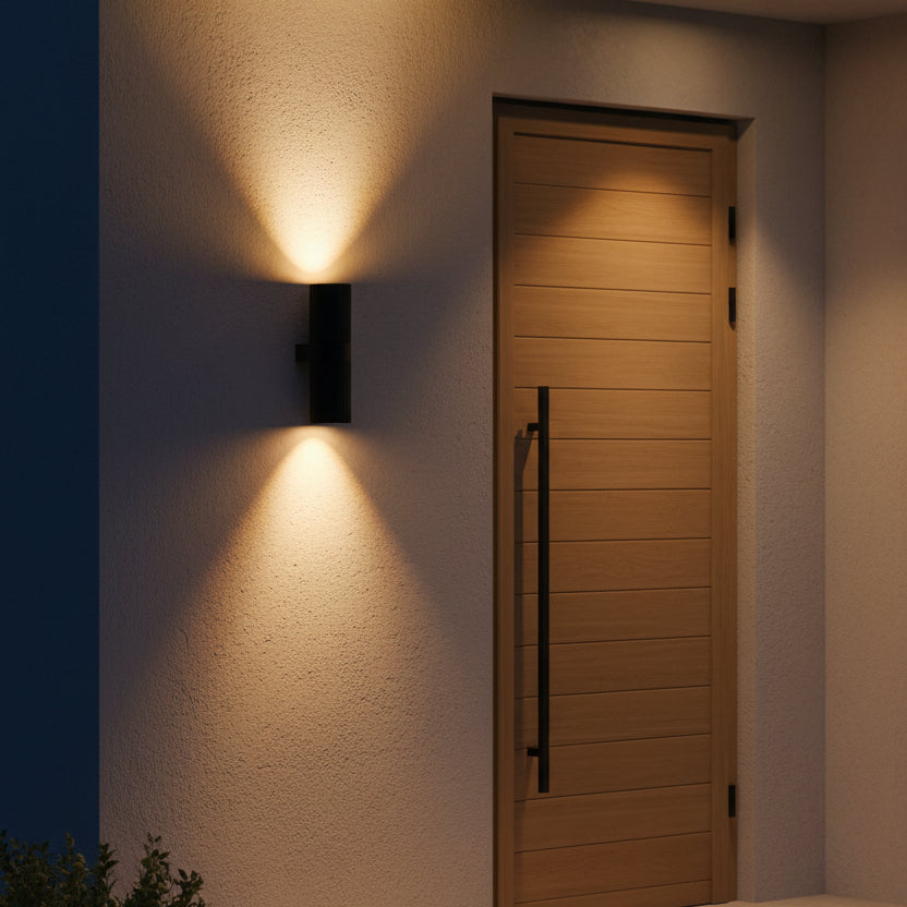 Black cylindrical outdoor wall light illuminating a textured wall and wooden door