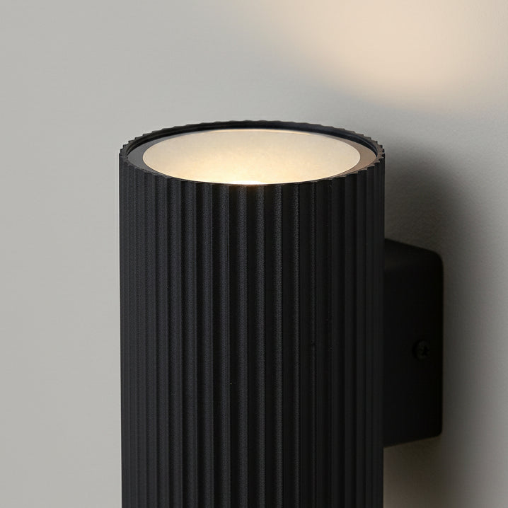 Black cylindrical wall light with ribbed texture, emitting light upwards and downwards