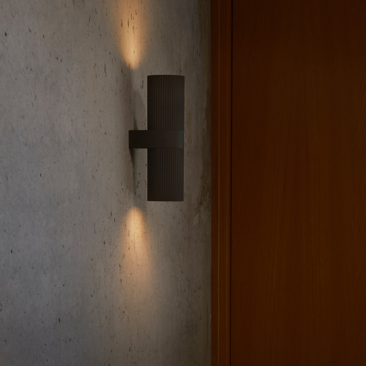 Dark grey fluted wall light on a concrete wall next to a wooden door