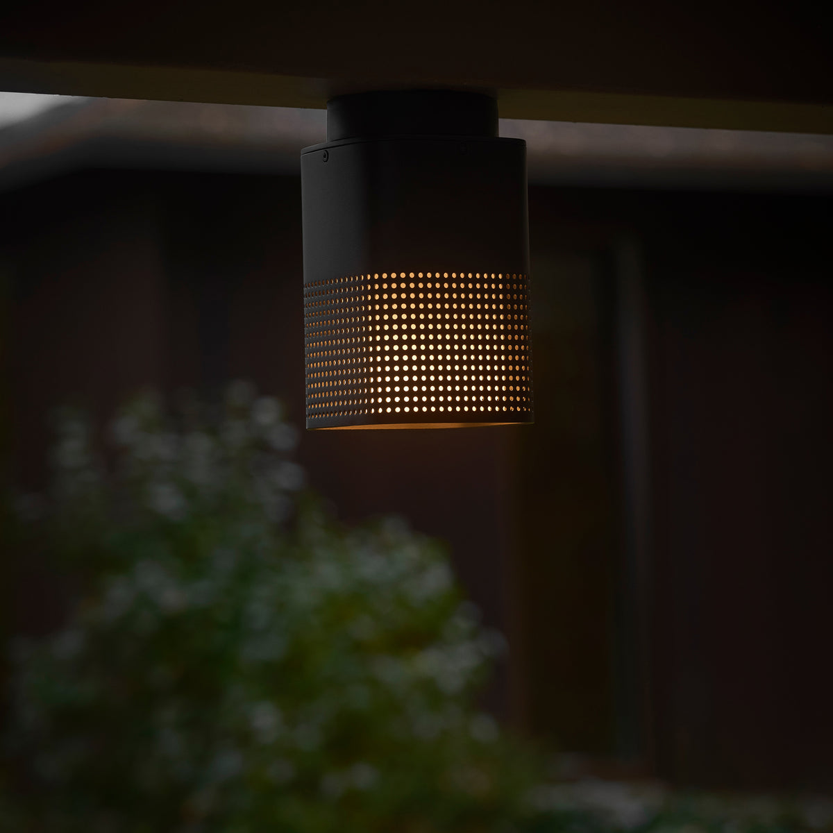 Black cylindrical light fixture with a perforated pattern emitting a warm glow