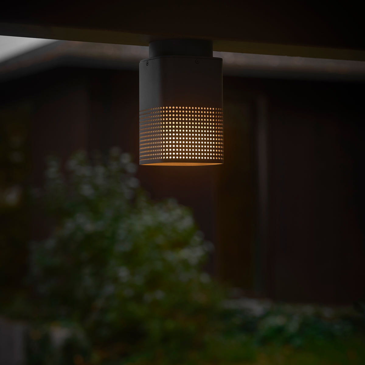 Close up of a dark grey outdoor light fixture with a perforated pattern, emitting a warm glow