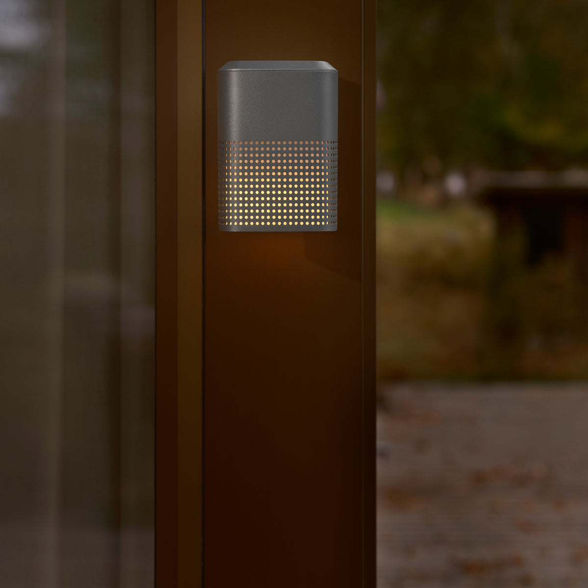 Dark grey outdoor wall light with a perforated pattern emitting warm light