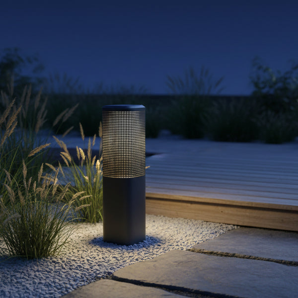 Outdoor bollard light illuminating a gravel path next to a wooden deck and tall grasses at night