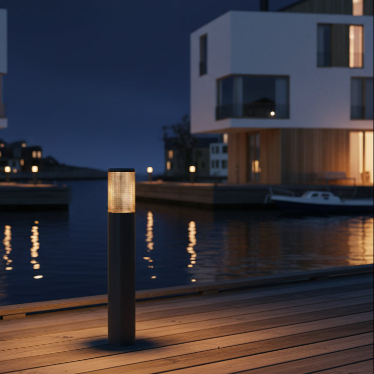 Bollard light on a wooden dock at night with modern buildings and water in the background