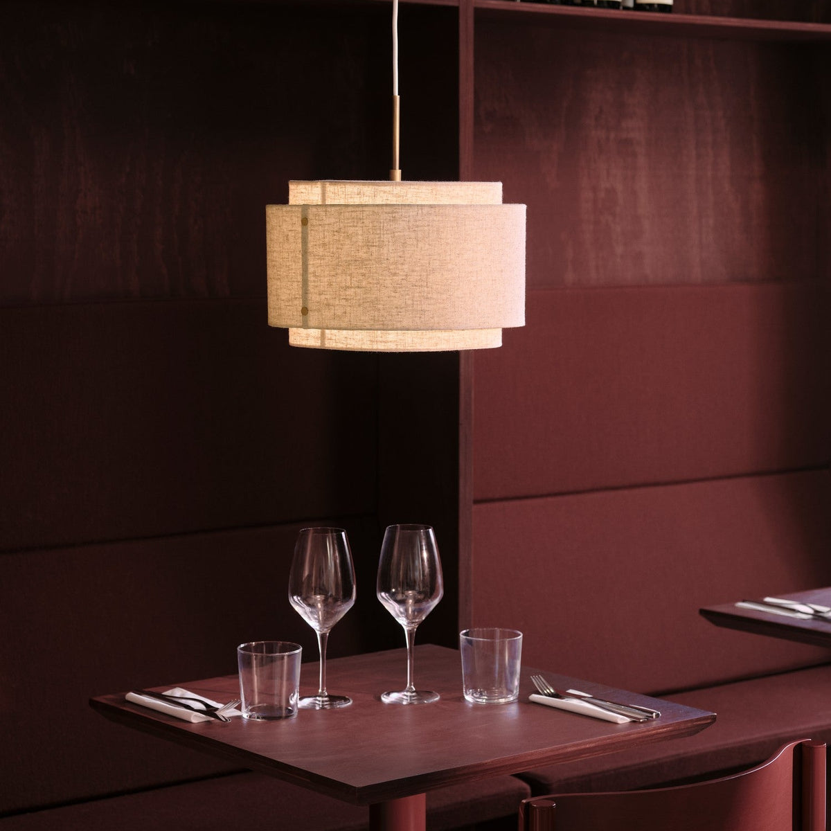 A restaurant table with two wine glasses, two water glasses, and cutlery on a dark red table