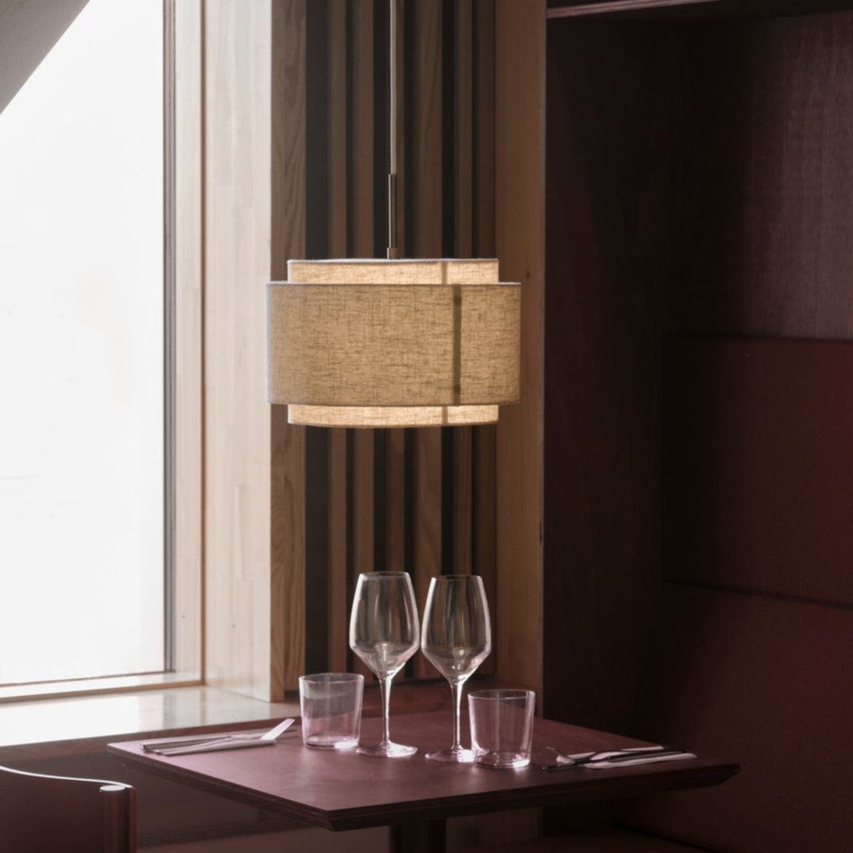 A dining table with two wine glasses, two water glasses, and cutlery, under a hanging fabric lamp