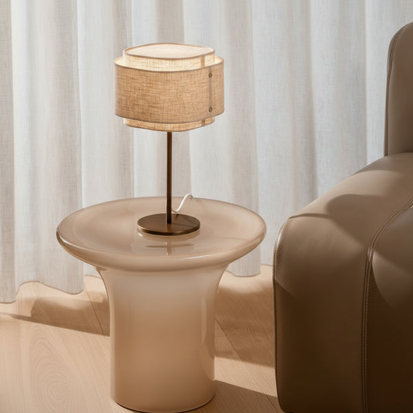 Table lamp with a two-tiered fabric shade on a mushroom-shaped side table next to a leather armchair