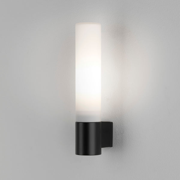 Black cylindrical wall light with a frosted white diffuser, illuminated against a light grey wall