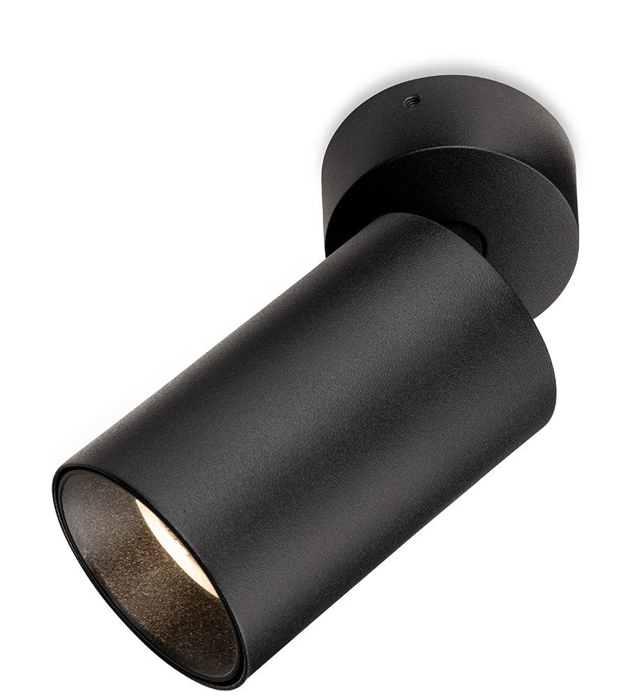 Black cylindrical ceiling spotlight with a textured finish, angled downwards, emitting a warm light