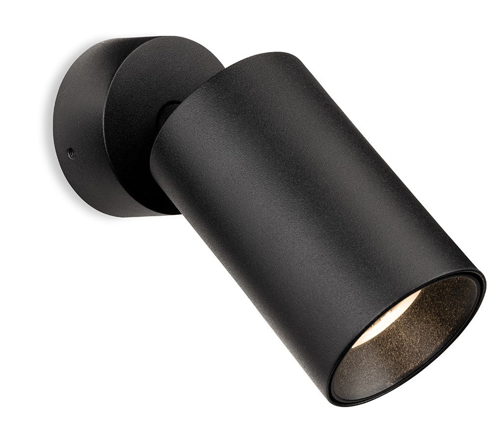 Black cylindrical wall-mounted spotlight with a textured finish, angled downwards and emitting a warm light