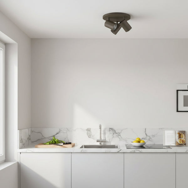 Three dark grey spotlights on a white ceiling above a kitchen counter with a sink and marble backsplash