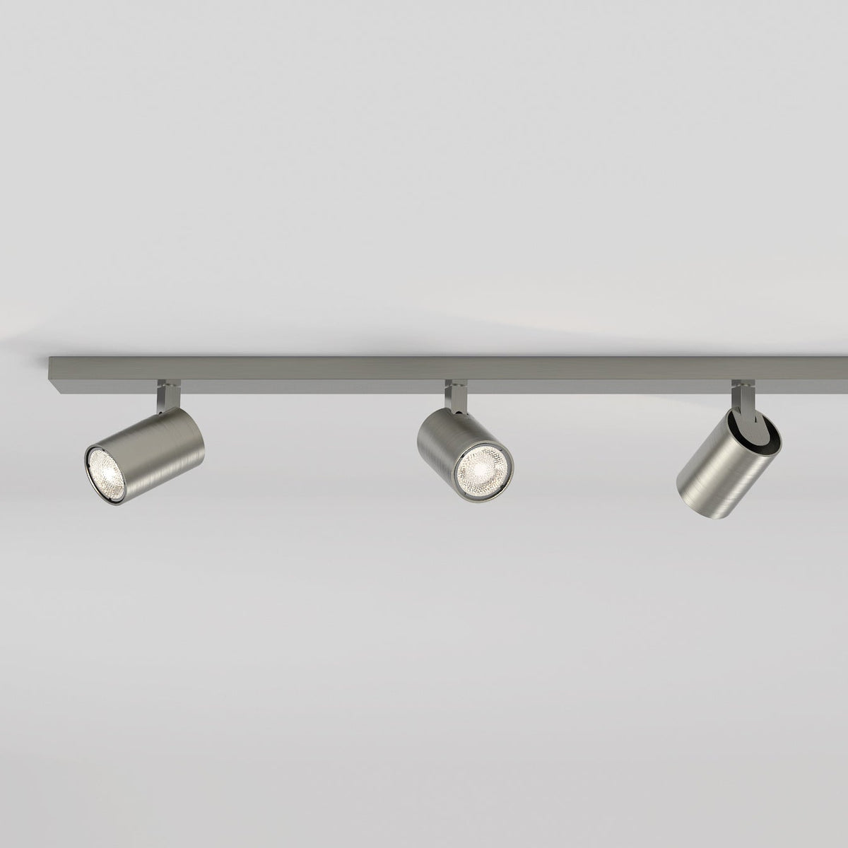 Three brushed metal cylindrical track lights on a grey track against a white ceiling