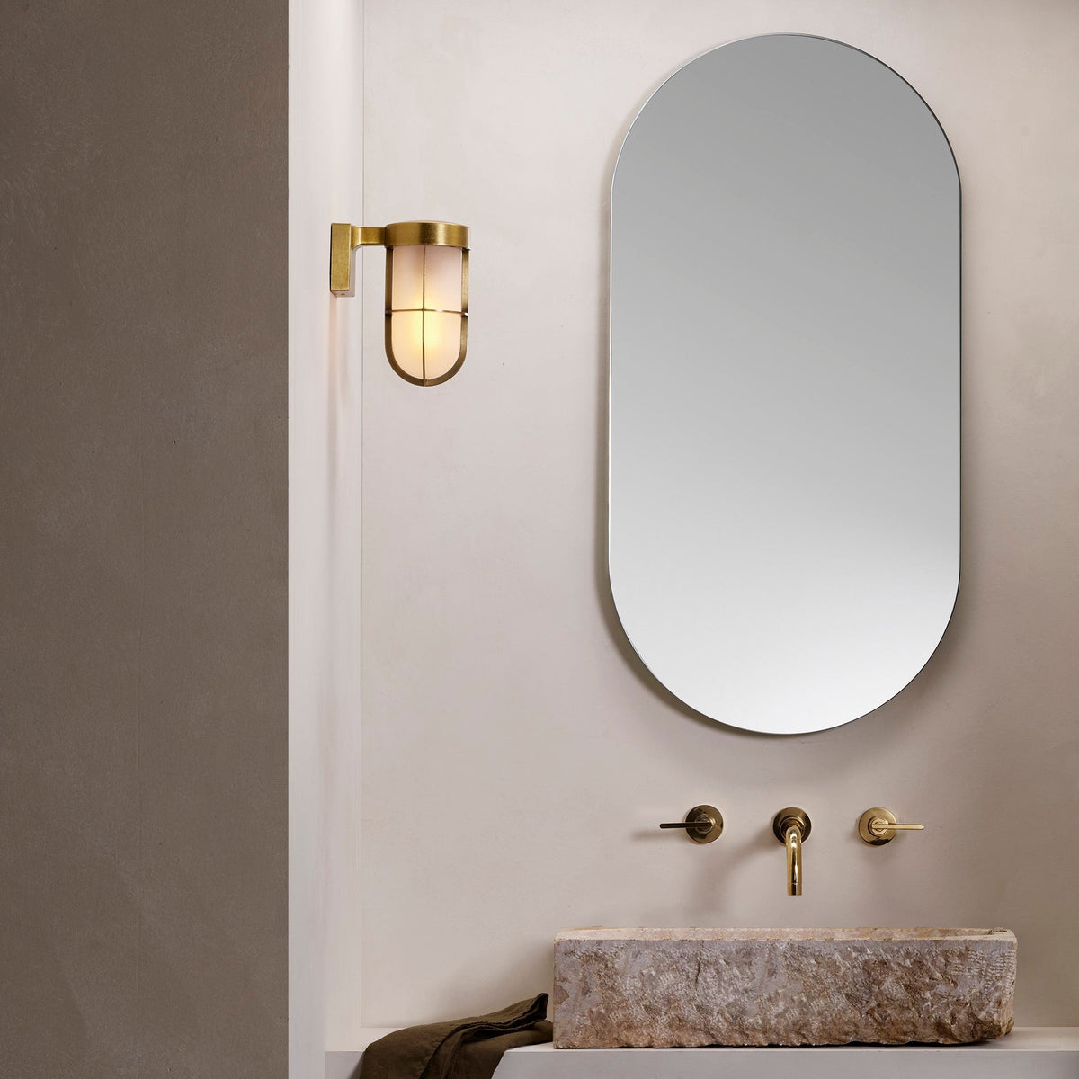 Bathroom with oval mirror, brass wall light, stone sink, and brass faucet