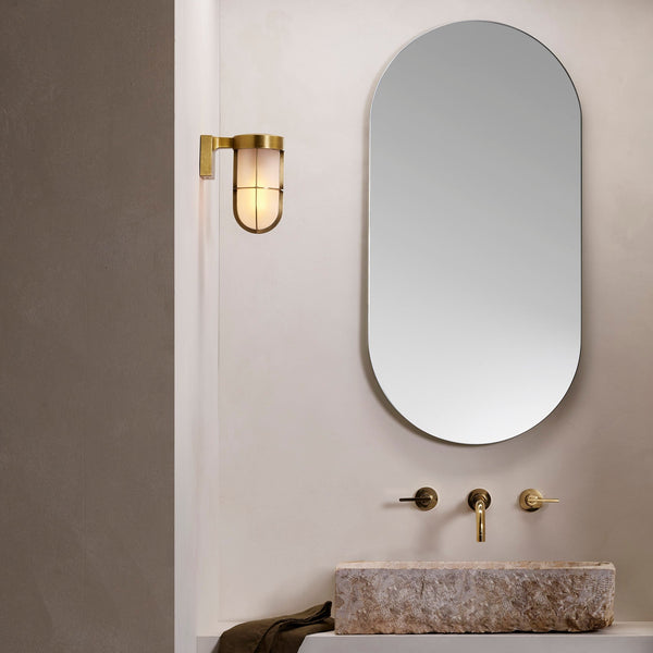 Bathroom with oval mirror, brass wall light, stone sink, and brass faucet