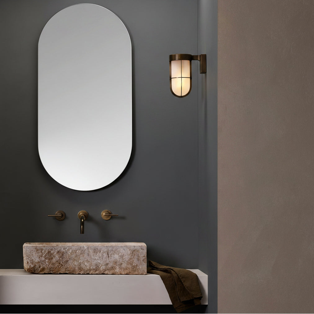 Oval mirror above a stone sink with brass faucet and wall-mounted light