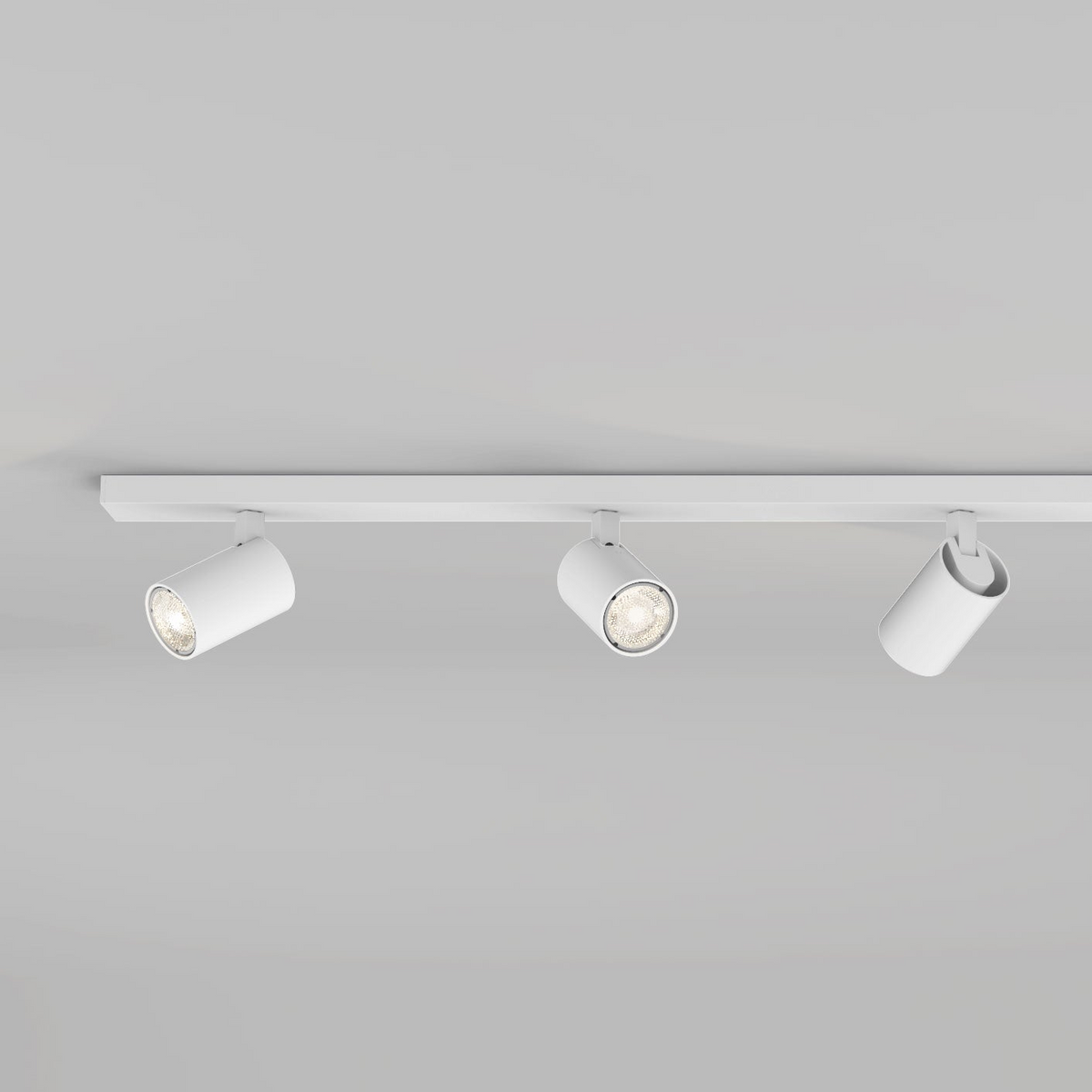 Three white cylindrical track lights on a white track against a light gray ceiling