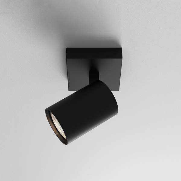 Black cylindrical ceiling spotlight with a square base, angled downwards, on a white textured ceiling