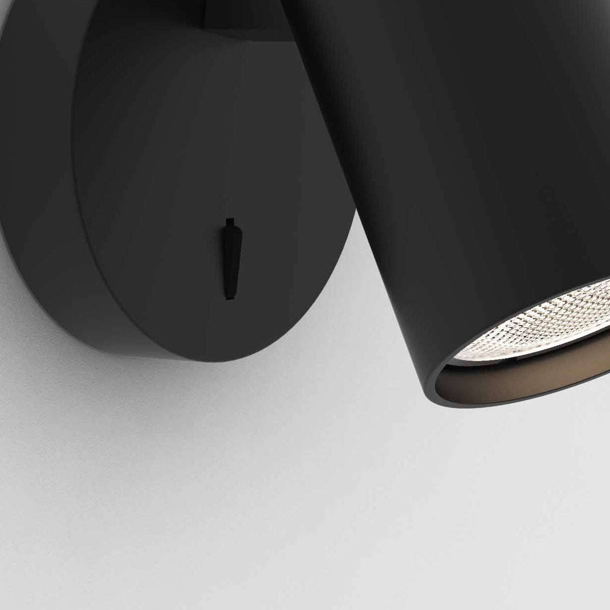 Black wall-mounted light fixture with a cylindrical spotlight and a small switch on the circular base