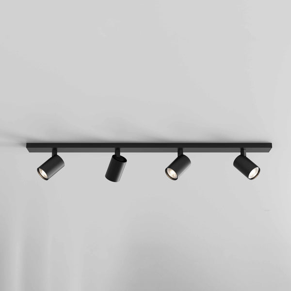 Four black track lights on a black bar, mounted on a white ceiling