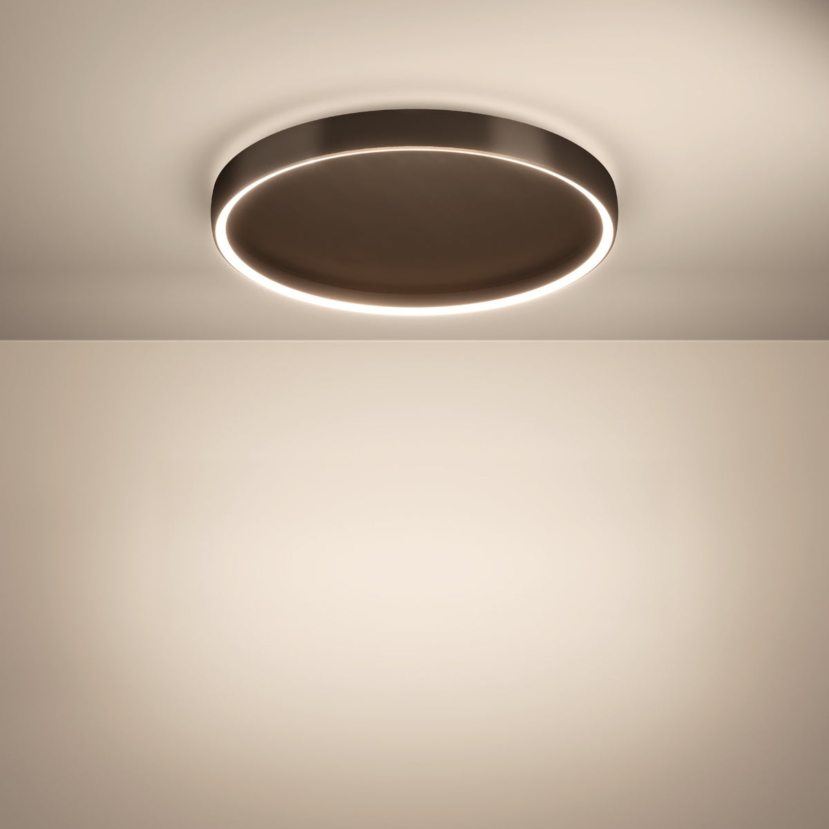 A round, dark bronze ceiling light with a glowing white inner ring illuminates a light beige wall.