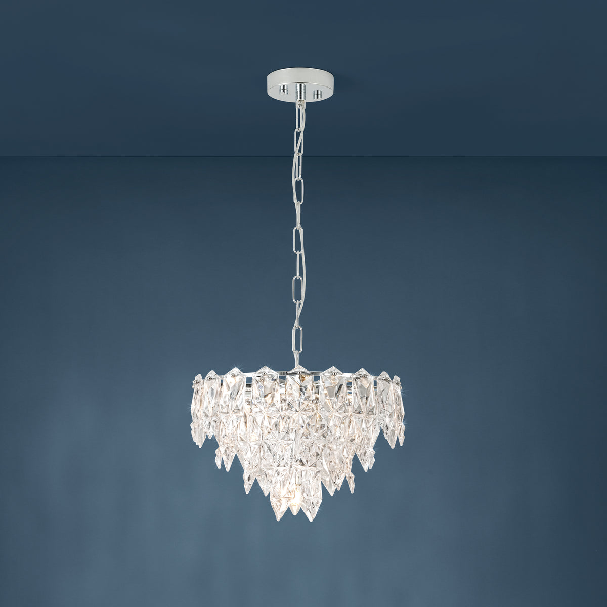 A sparkling crystal chandelier with a chrome finish hangs against a dark blue wall.