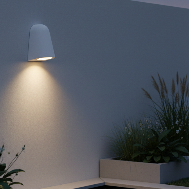 White outdoor wall light illuminating a textured wall above a planter with tall grasses and small white flowers