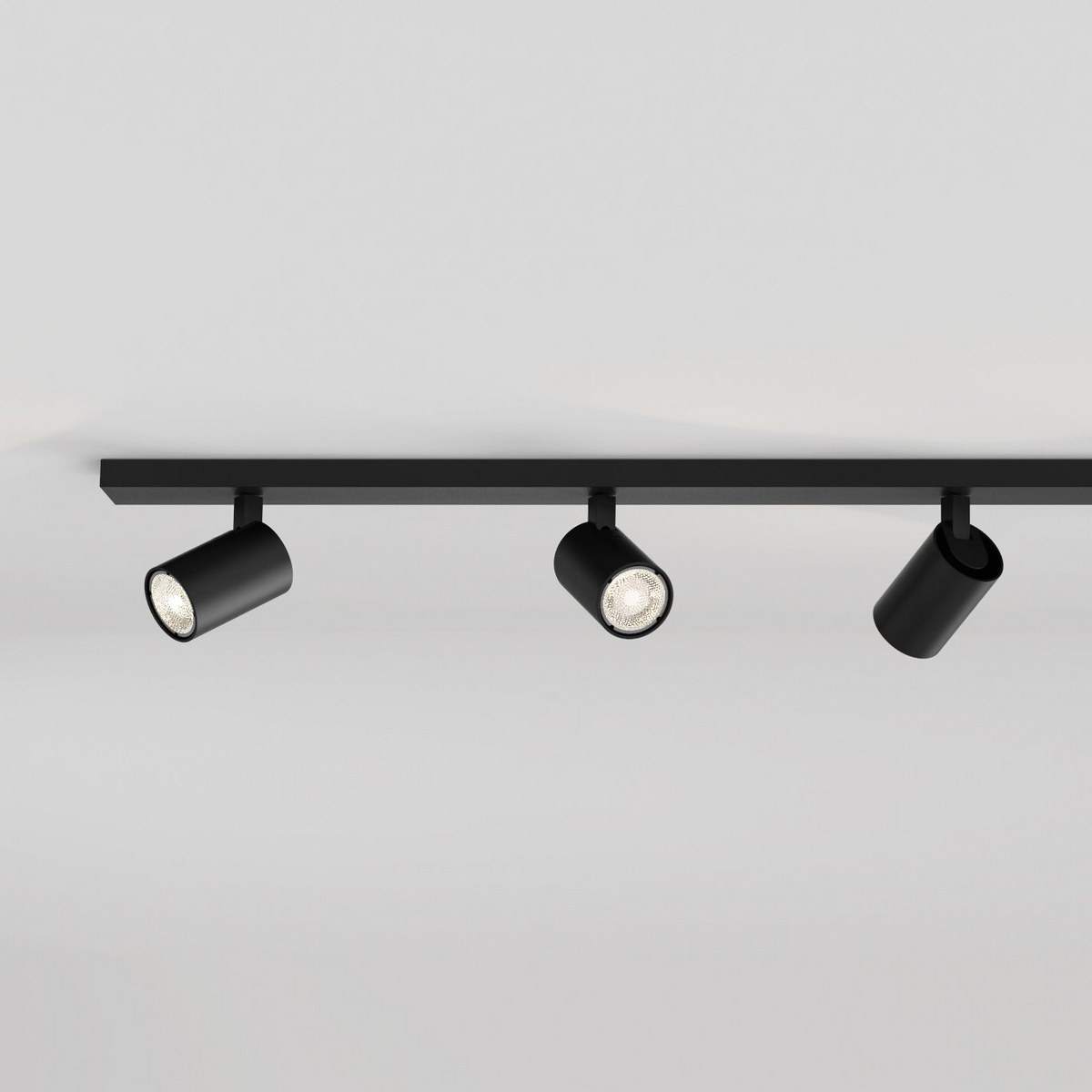Three black track lights on a black rail against a white ceiling